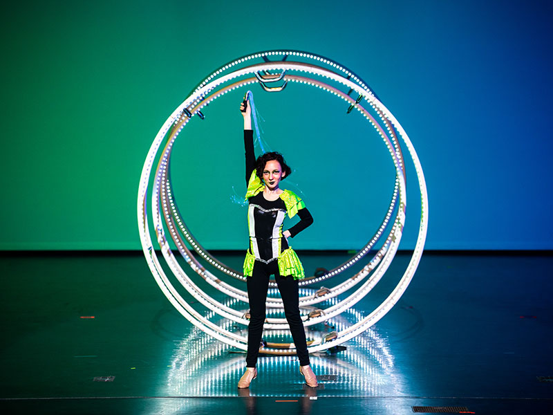 Circus performer posed in front of lighted rings.