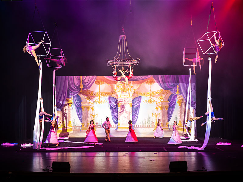 Elaborate stage scene with costumed aerial performers and dancers.